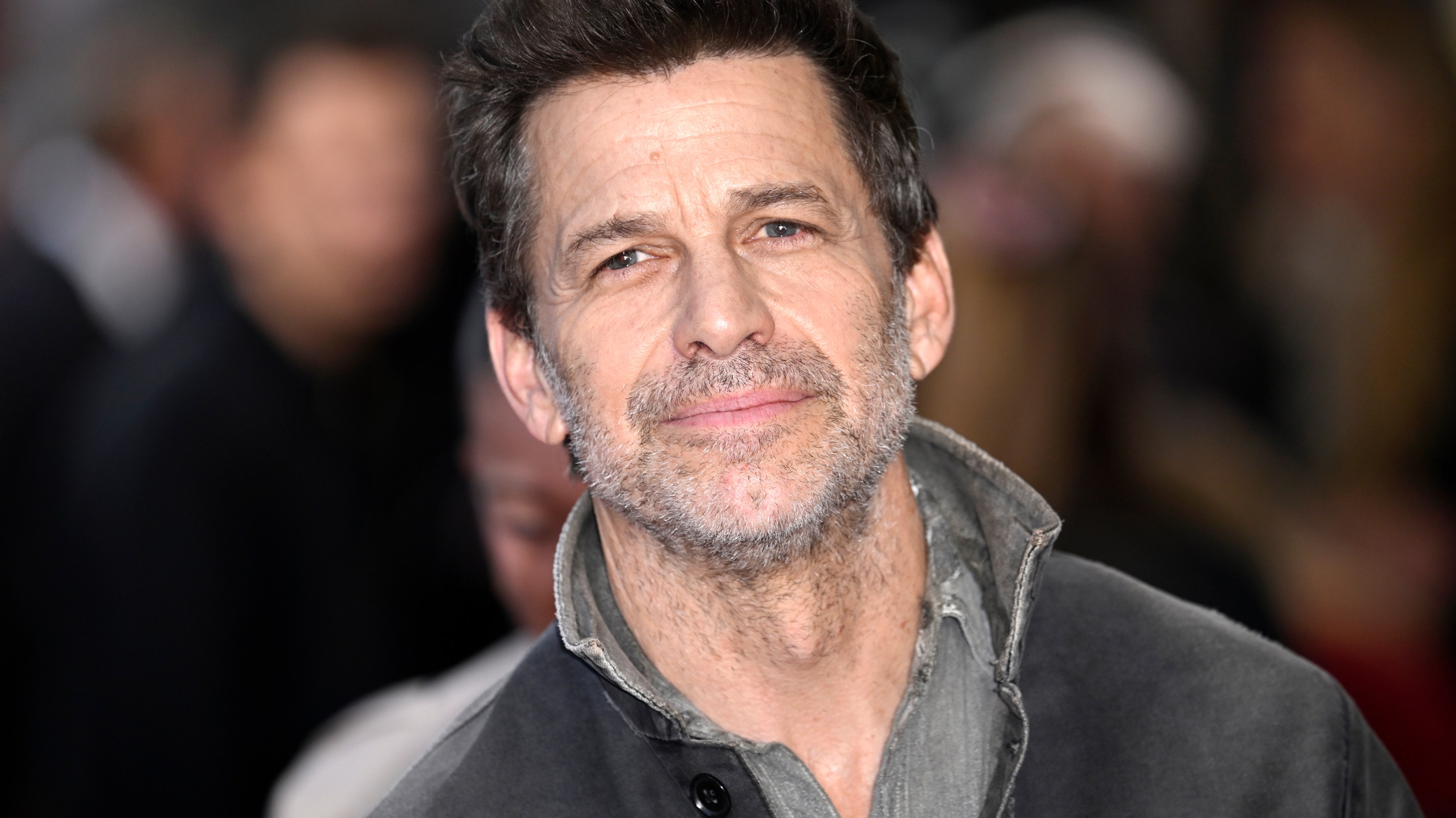 Le réalisateur Zack Snyder porte un quart de zip gris foncé.