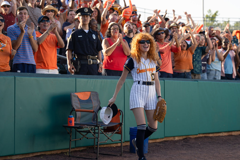 Poker Face Season 2 Stars Natasha Lyonne comme Charlie Cale, qui est montré comme une balle dans un match de baseball ici, portant des uniformes rayés avec des gants et une chaussette noire haute 