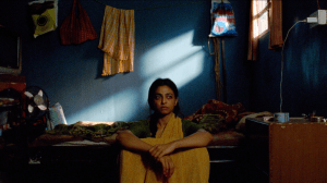 Une femme dans un saren jaune qui est assis à côté de son lit avec un regard sur le sol; Radhika apte dans le film 